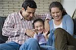 Parents sitting on a couch and tickling their daughter