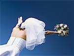 Low angle view of a bride holding a bouquet of flowers with her arms raised