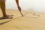 Vue en coupe basse d'une personne de dessiner un coeur dans le sable sur la plage