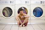 Man sitting in boxers at Laundromat checking watch