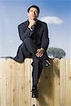 Businessman sitting on fence looking up