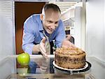 Man in refrigerator with green apple reaching for chocolate cake