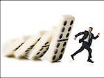 Businessman running from falling dominoes