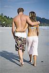 Rear view of a young couple with their arms around each other walking on the beach