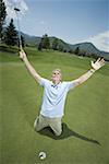 Homme à genoux près d'un trou de golf avec les bras levés