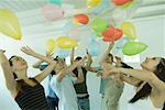 Group of young friends hitting balloons floating in the air