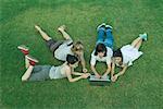 Groupe de jeunes amis couché sur l'herbe, à l'aide d'ordinateur portable