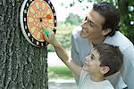 Man and boy looking at dartboard hanging on tree