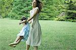 Woman swinging daughter around on grass