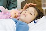 Girl sleeping in hospital bed, woman's hand posed over girl's forehead