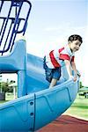 Boy on playground equipment, smiling, looking away