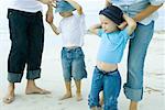 Parents putting sunhats on children at the beach, low section