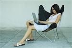 Frau im Sessel mit Laptop, in voller Länge