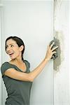 Woman wiping grout on wall with wet rag, looking over shoulder