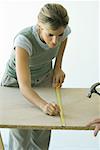 Woman using measuring tape to draw line on wood board