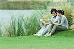 Young adult couple reading outdoors, sitting on grass by edge of lake
