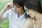 Young couple sitting close together, man using cell phone