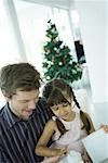 Girl sitting on father's lap, opening Christmas present