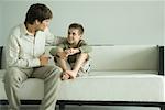 Father and son sitting on sofa, talking