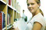 Female college student standing by shelves in library