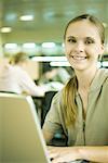 Female college student sitting at table in library, using laptop