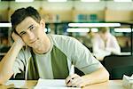 Male college student sitting in library, smiling at camera