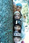 Kids and teens peeking from behind tree in ski clothes, portrait