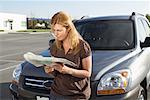 Femme debout devant la voiture, en regardant la carte routière