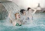 Young people standing under water spray in spa pool