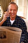 Mature man reading newspaper and talking on cell phone