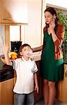 Woman talking on cell phone and boy doing bubble with gum in the kitchen