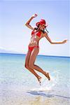 Young woman in bikini and hat jumping in the air