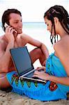 Young couple on beach with laptop and cell phone