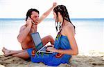 Young couple on beach with laptop and cell phone