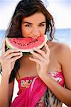 Young woman on beach eating watermelon