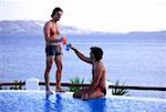 Two men toasting with cocktails by the poolside