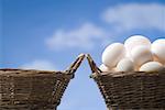 One empty basket and one basket filled with eggs outdoors with blue sky
