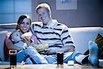 Man on sofa with woman feeding baby and bowl of popcorn smiling