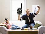 Woman on sofa and man in football jersey standing and cheering