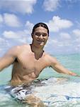 Man sitting on surfboard in water smiling