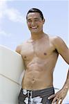 Mann mit Surfbrett am Strand lächelnd