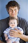Homme tenant un bébé garçon carré pour caméra souriants