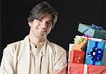 Portrait of a young man smiling with a stack of gifts beside him