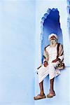 Low angle view of a senior man sitting on an arch window, Pushkar, Rajasthan, India