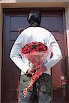 Rear view of a man hiding a bouquet of flowers behind his back