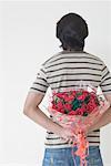 Rear view of a man holding a bouquet of flowers behind his back