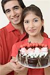 Portrait of a young couple holding a chocolate cake and smiling