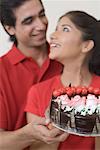 Close-up of a young couple holding a chocolate cake and looking at each other
