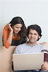 Junger Mann mit einem Laptop mit einer jungen Frau, die hinter ihm stehen