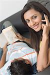 Portrait of a young woman talking on a mobile phone beside a young man reading a novel